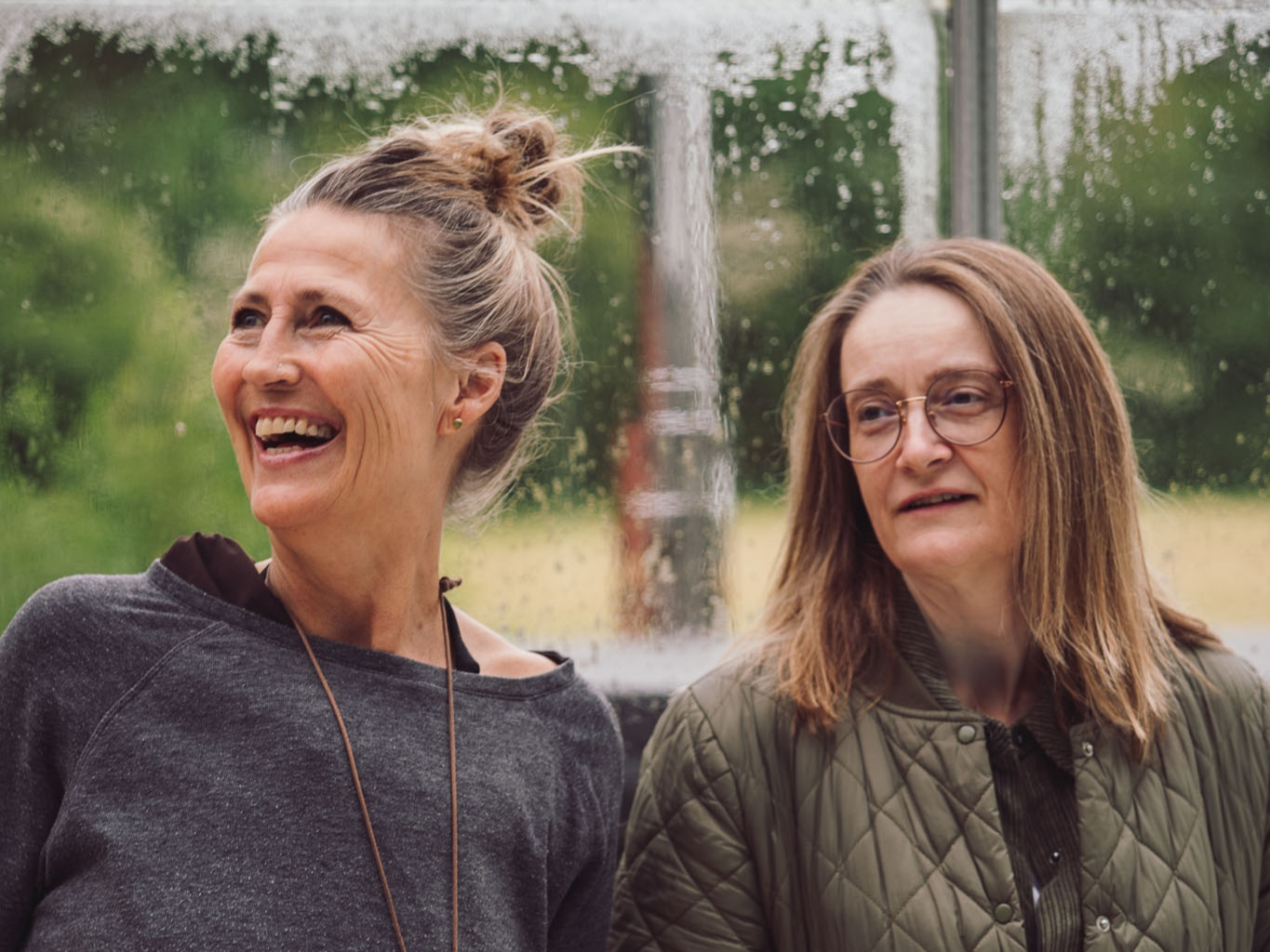 To personer står i et lyst drivhuslignende rum med dug på ruderne under en øvelse på Tobias‑Skolen, omgivet af grøn natur og et roligt læringsmiljø.