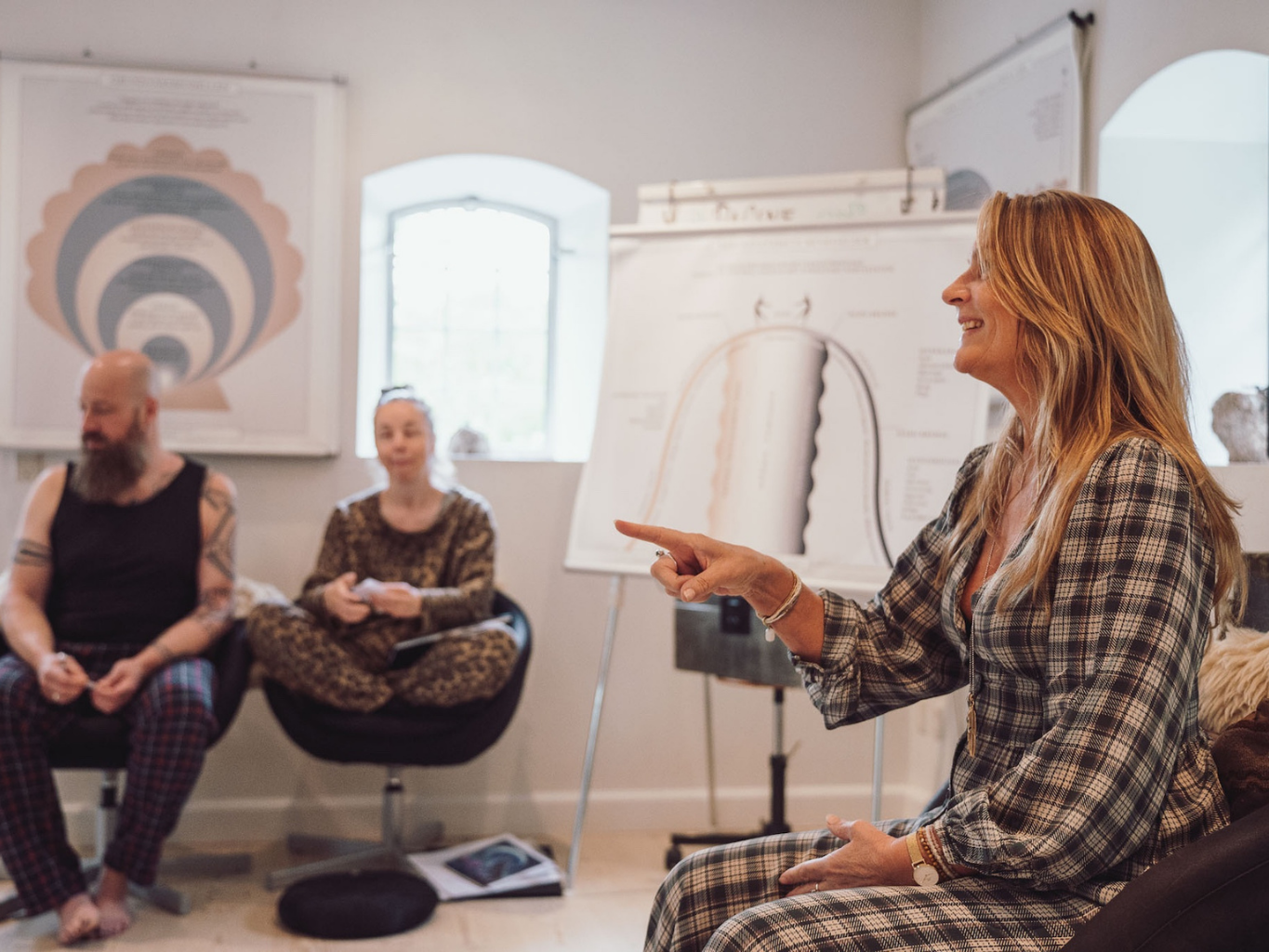 Undervisningssituation på Tobias‑Skolen, hvor en person sidder forrest og gestikulerer mod to deltagere i et lyst undervisningslokale med faglige plancher og whiteboard.