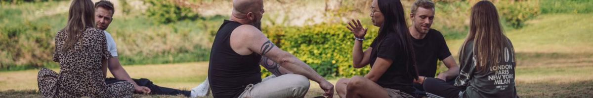 Studerende på psykoterapeutuddannelse sidder i grupper udendørs i naturskønne omgivelser og deltager i dialog, refleksion og fællesskab på Tobias-Skolen.
