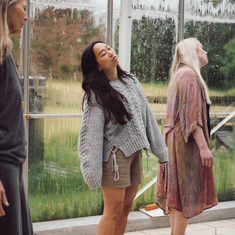 Flere personer står i et lyst drivhuslignende rum med store glasvægge, omgivet af grøn natur, under en øvelse på Tobias‑Skolen.