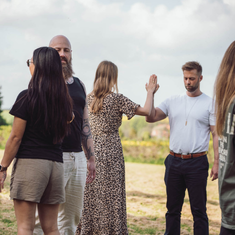 Gruppe af mennesker deltager i udendørs øvelse og giver high‑five i trygge, grønne omgivelser – illustrerer fællesskab, nærvær og relationsarbejde som en del af Tobias‑Skolens psykoterapeutuddannelse, kurser og efteruddannelser.
