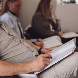 Personer i undervisningslokale, der fordyber sig i læsning og note­skrivning under psykoterapeutisk undervisning – stemningsbillede der viser læring, refleksion og faglig udvikling på Tobias‑Skolens psykoterapeutuddannelse og efteruddannelser.
