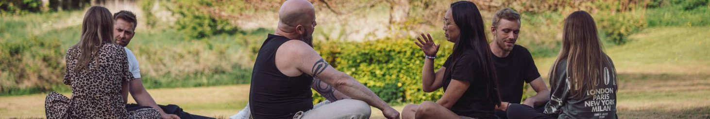 Gruppe af mennesker siddende i cirkel i naturen under en nærværende dialog – illustrerer fællesskab, tryghed og personlig udvikling som en del af Tobias‑Skolens psykoterapeutuddannelse, kurser og efteruddannelser.